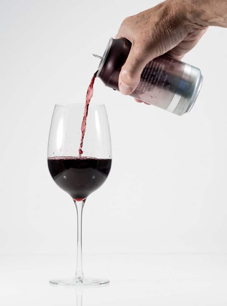 un homme verse une canette de vin dans un verre à pied.