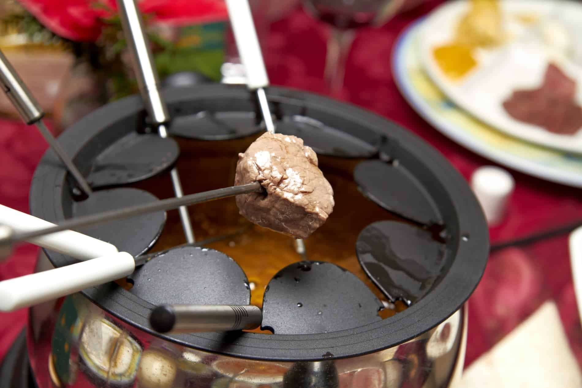 Morceau de viande plongé dans une fondue bourguignonne accompagné de vin rouge